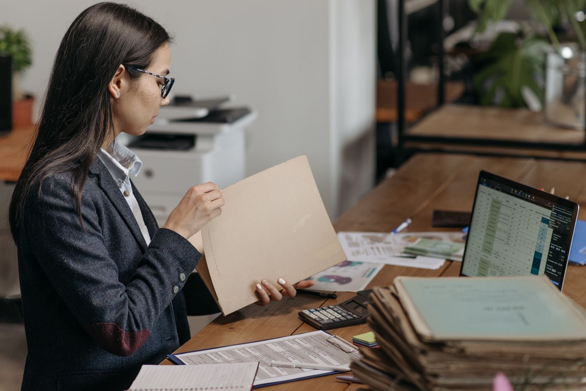 A professional reviewing documents at her office desk with a laptop and files.